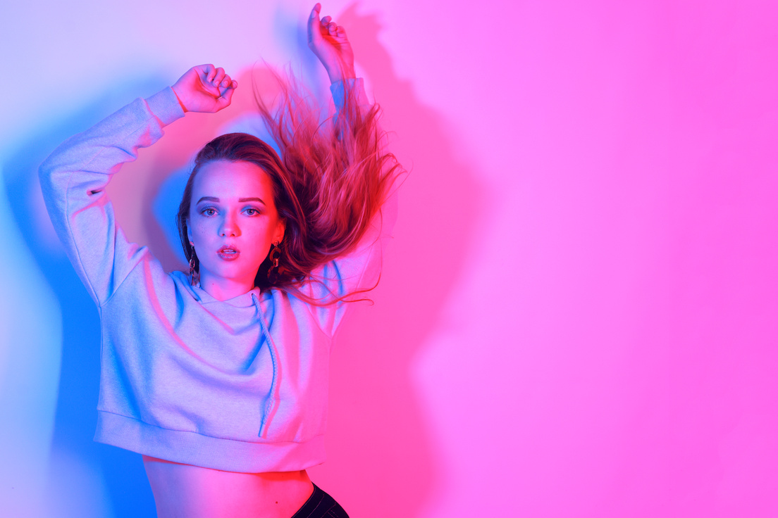 Fashion portrait of young elegant girl. Colored neon background, studio shot. Beautiful brunette woman. Hipster girl dancing in neon. Woman with stylish hair and red lips. Girl in a sweater and long hair.